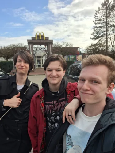 Drei junge Filmemacher, Doran Urban, Gerrit Kock und David Melüh, stehen lächelnd vor einem McDonald's Restaurant. Dieser Ort markiert die Gründung ihrer Filmemachergruppe funeralhomefilms.