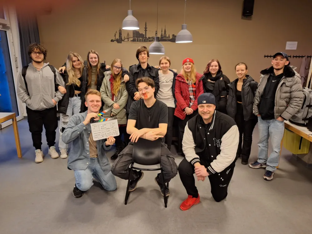 Gruppenfoto von Crew und Darstellern am Set, alle lächeln und zeigen ihre Begeisterung für das Filmprojekt.