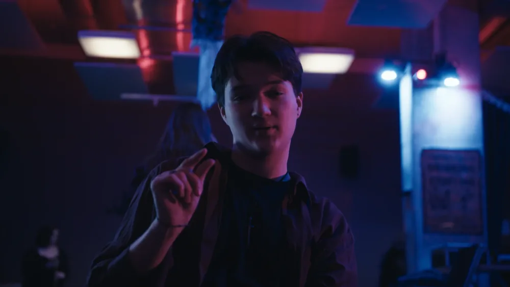 Szene in einem Nachtclub mit tanzenden Menschen und leidenschaftlicher Stimmung, farbiges Licht sorgt für intensive Atmosphäre.