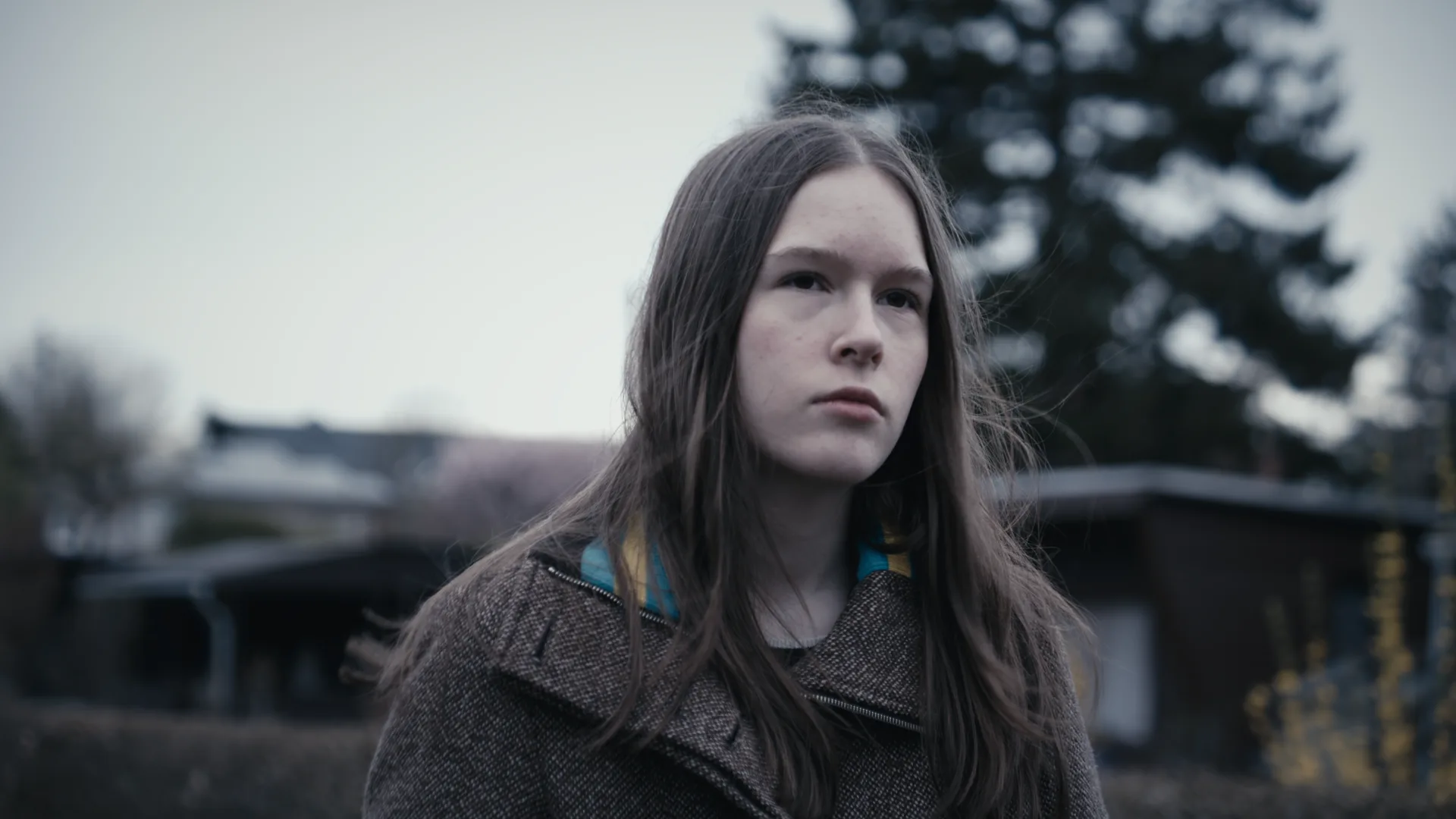 Filmstill einer Protagonistin, die unbeirrt und gedankenversunken in die Ferne blickt, der Hintergrund ist unscharf.