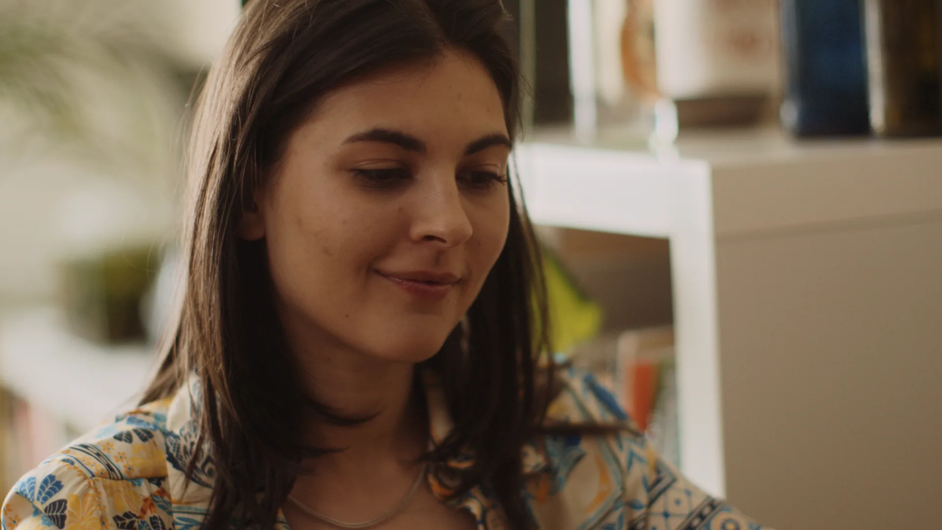 Alt-Text: Filmszene mit einer jungen Frau als Darstellerin, die ernst in die Kamera blickt. Sie steht in einem hellen Raum, der Hintergrund ist unscharf gehalten.