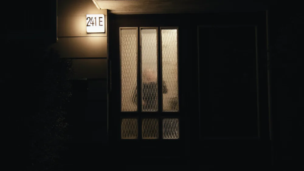 Nachtszene mit geheimnisvoll beleuchteter Tür, Schatten und Licht erzeugen eine spannungsgeladene Atmosphäre.