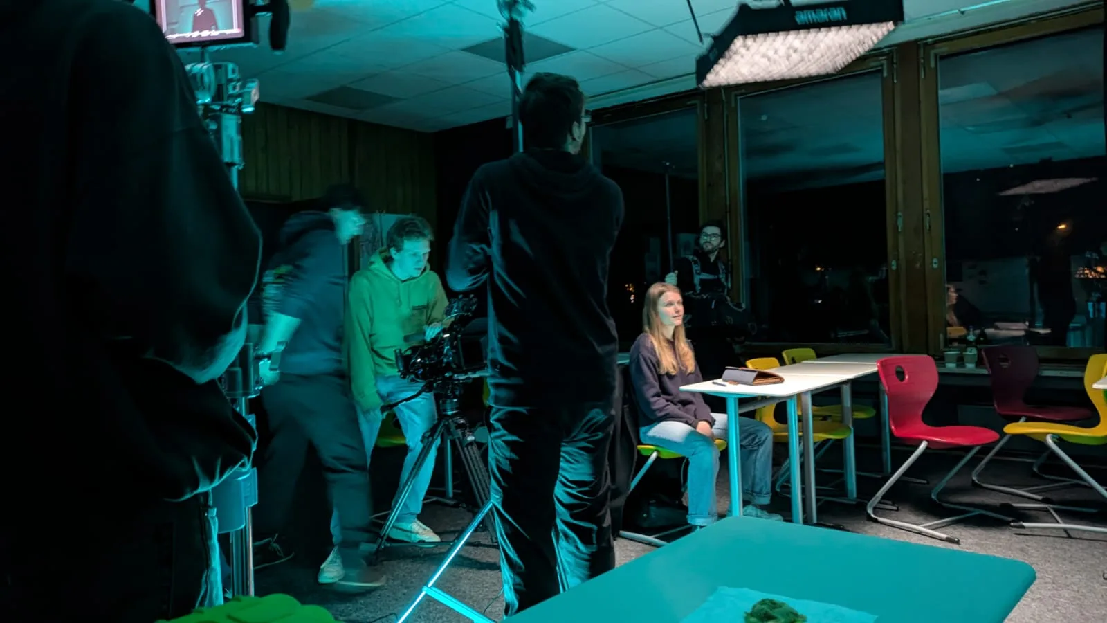 Produktionsteam am Set von „Crisis“ arbeitet unter türkisfarbener Lichtstimmung, Filmtechnik und Crew sind im Raum verteilt.